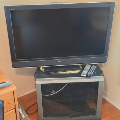 Sony Bravia flat-screen television with two remote controls, resting on a modern silver and black glass-door media stand.