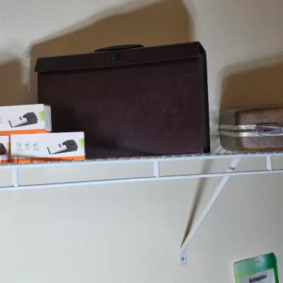 Vintage brown expanding file folder and a hard-shell briefcase displayed on a wire shelf alongside boxed door stop alarms.