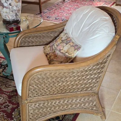 Vintage woven rattan armchair with white cushions and a cat-themed tapestry accent pillow.