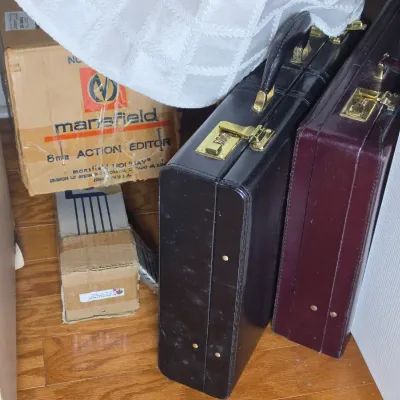 Two vintage hard-sided briefcases, one black and one burgundy, with brass combination locks, shown alongside a boxed Mansfield 8mm Action...