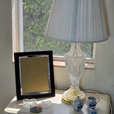 Vintage cut crystal table lamp with a brass base and pleated white shade, displayed alongside a dark wood picture frame and small...