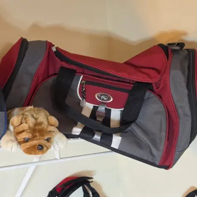 California Pak red and gray duffel bag with black straps, shown alongside a small plush dog toy on a wire shelf.
