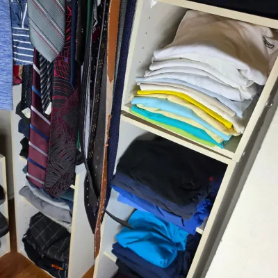 Assorted men's clothing, including folded shirts, hanging neckties, belts, and shoes, organized in a white closet shelving unit.