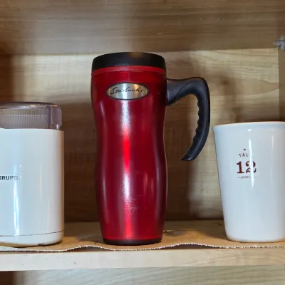 Krups electric coffee grinder in white, paired with a red metallic Starbucks travel mug and a white ceramic Starbucks 12-ounce mug.