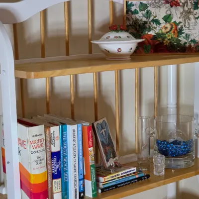 Two-tier wooden baker's rack with white painted frame and natural wood shelves, holding cookbooks, a glass ice bucket, and...