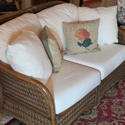 Woven rattan and wicker loveseat featuring a curved back, white cushions, and decorative accent pillows.