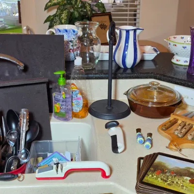 Assorted kitchenware including a wooden knife block with knives, a brown glass casserole dish, a black paper towel holder, and various...