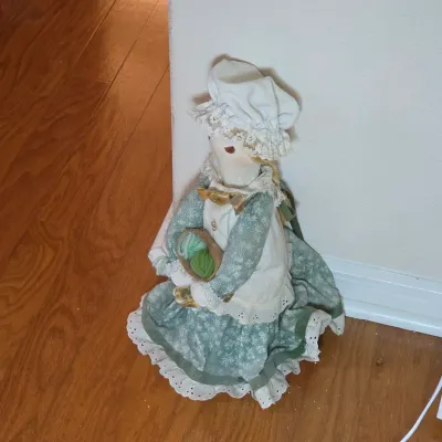 Vintage handmade fabric doll dressed in a green floral dress, white apron, and matching bonnet, holding a small basket of yarn.