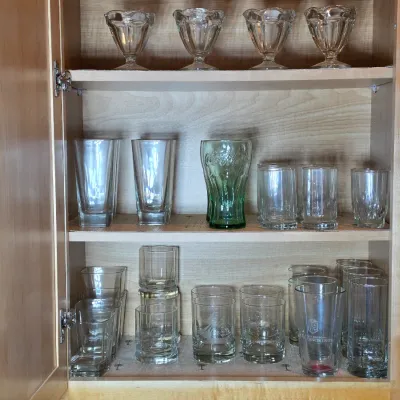Assorted glassware collection, including sundae dishes, tall tumblers, a green Coca-Cola glass, and various drinking glasses, arranged...