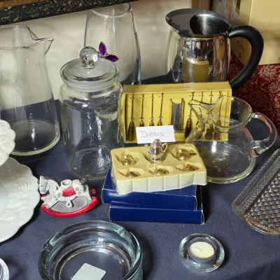 Assorted glassware and tabletop items, including a clear glass pitcher, a lidded jar, a small silver-tone tea set in packaging, and a...