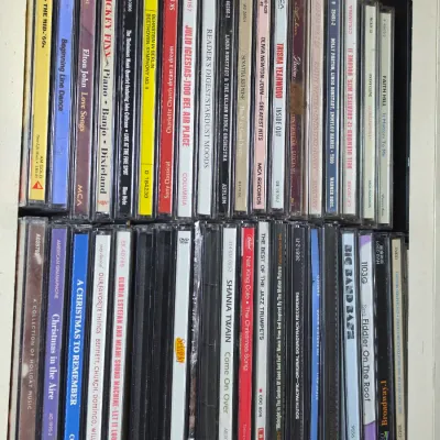 A collection of assorted music CDs in jewel cases, featuring various genres including country, pop, classical, and holiday music.