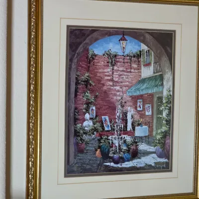 Framed impressionistic art print depicting a European courtyard scene, presented in an ornate gold-finished frame with a double mat.