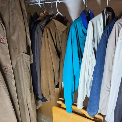 Assorted vintage outerwear hanging in a closet, including a long brown suede coat, a teal windbreaker, and a denim jacket.