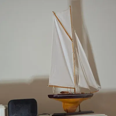 Vintage wooden model sailboat with white fabric sails, displayed on a matching wooden stand.