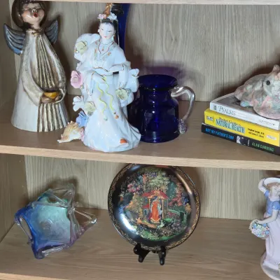 Assorted decorative collectibles displayed on wooden shelves, including porcelain figurines, a cobalt blue glass pitcher, a Russian...