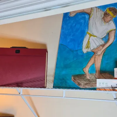 An original painting on canvas depicting an ancient Greek discus thrower, displayed alongside a red expanding file folder and small boxed...