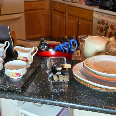 Assorted kitchenware including floral-patterned creamers and sugar bowls with gold trim, a stack of mid-century ceramic plates, and...