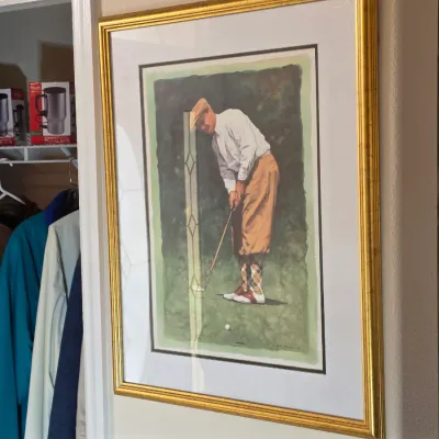 Framed vintage-style golf print depicting a golfer in classic attire, presented in a matted gold-finished frame.