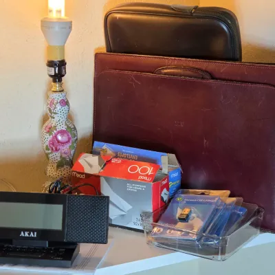 Assorted office and desk items, including a vintage Akai digital alarm clock, a floral ceramic table lamp, a burgundy leather briefcase,...