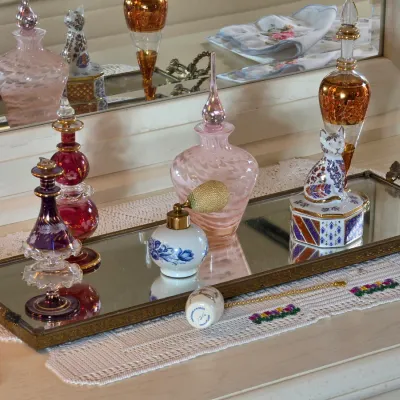 Collection of vintage glass and porcelain perfume bottles, including a pink swirl glass bottle and a porcelain cat figurine, displayed on...