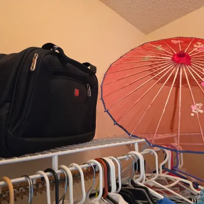 Wenger SwissGear black nylon travel bag alongside a decorative red paper parasol with floral details, displayed on a closet shelf.