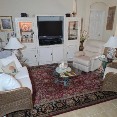 Living room furniture set featuring a wicker-framed sofa and armchair with white cushions, a cream-colored leather recliner, a glass-top...