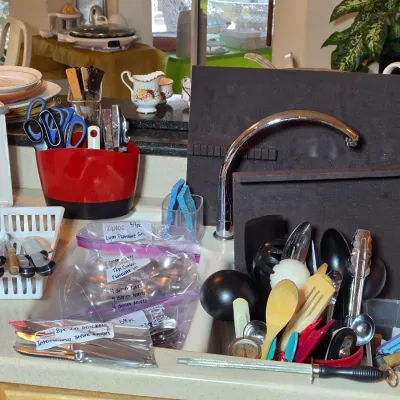 Assorted kitchenware and utensils, including flatware sets in plastic bags, a knife sharpener, wooden spoons, and a Black & Decker...