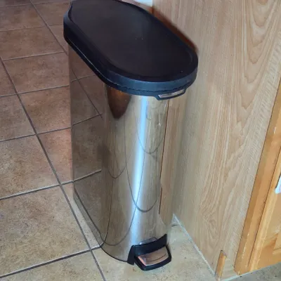 Slim stainless steel step trash can with a black plastic lid, designed for space-saving kitchen placement.