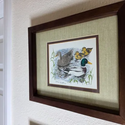 Framed mallard duck print by artist Philip Scholer, dated 1983, featuring a burlap-textured mat and a dark wood frame.