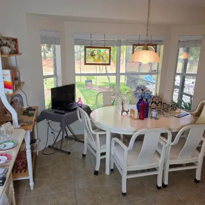 Casual dining set featuring a round white laminate table and five matching white wooden armchairs on casters, shown alongside various...
