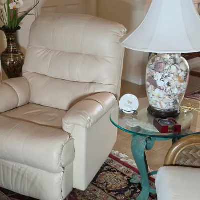 Cream-colored leather recliner paired with a glass-top side table featuring a seashell-filled table lamp.