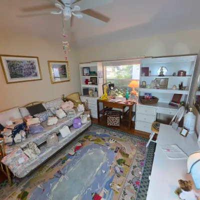 A bedroom featuring a brass daybed piled with linens, a white hutch desk, a smaller wooden writing desk, and a colorful pictorial area rug.