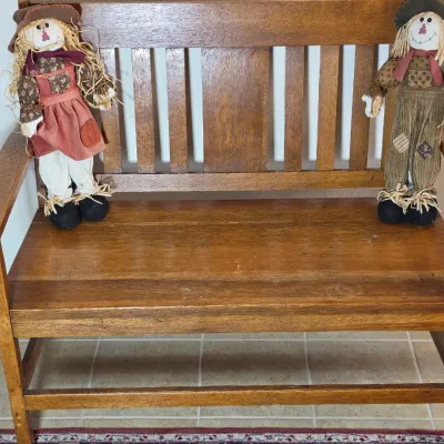 Mission-style oak bench with a slatted back, decorated with two fabric scarecrow dolls.