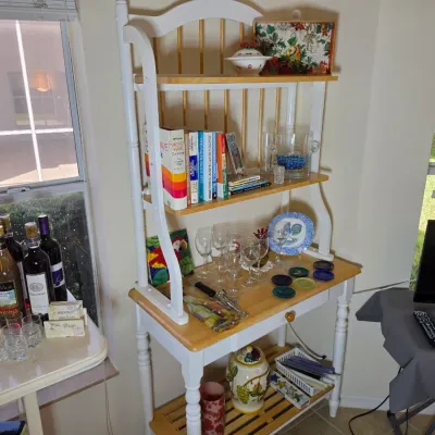 Country-style wooden baker's rack with a white painted frame, natural wood shelves, and spindle back details, displaying various...