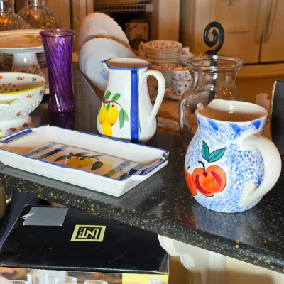 Assorted ceramic and glass kitchenware, including a hand-painted lemon pitcher and matching tray, a blue-speckled apple pitcher, and a...