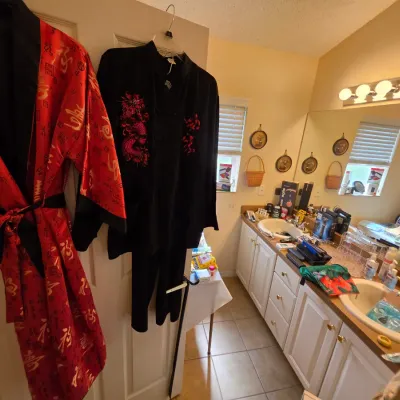 Red satin robe with gold Asian characters and a black two-piece pajama set featuring red dragon embroidery, hanging on a door in a bathroom.