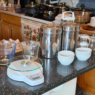 Assorted kitchenware including a Conair digital kitchen scale, Pyrex and Oven Basics glass measuring cups, stainless steel canisters, and...