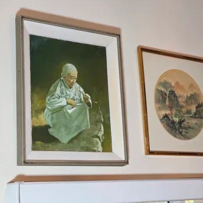 Two framed East Asian artworks, including an oil painting depicting an elder smoking a pipe and a circular landscape print in a...