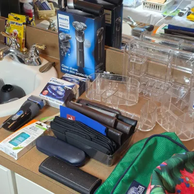 Assortment of personal care items, including a Philips Norelco shaver in its box, clear acrylic makeup organizers, wallets, and grooming...