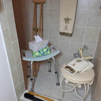 Adjustable medical shower chair with a textured seat, shown alongside a decorative metal vanity stool and a pair of wooden crutches.