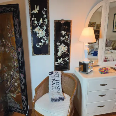 Vintage bedroom set featuring a white laminate dresser with an arched mirror, a cane-back barrel chair, and Asian-inspired decor...