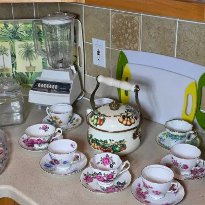 Vintage kitchenware collection featuring an enamel tea kettle with fruit motif, several floral teacups with saucers, a vintage Osterizer...
