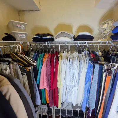 A well-organized closet featuring a variety of men's clothing, including dress shirts, polo shirts, trousers, and ties, alongside...