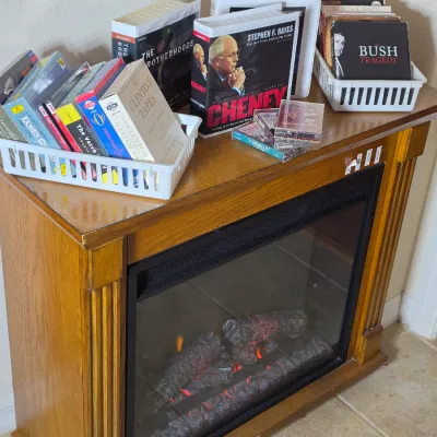 Electric fireplace heater in a light oak finish cabinet, shown with various audiobooks and media displayed on top.