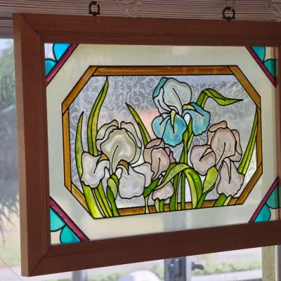 Stained glass window panel featuring an iris floral design, housed in a simple wooden frame with hanging hardware.