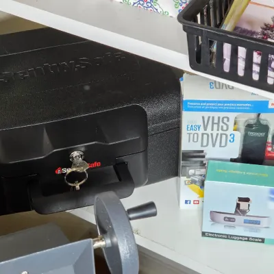 SentrySafe black fire-resistant chest with key included, displayed alongside a boxed Roxio Easy VHS to DVD 3 converter and an electronic...