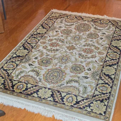 Traditional Persian-style area rug featuring a floral and palmette design in cream, sage green, and navy blue with fringed ends.