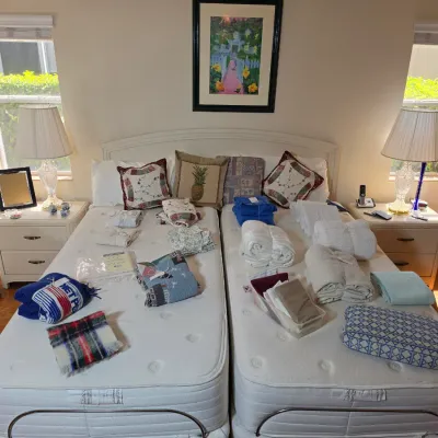 Pair of twin-size adjustable beds with white headboards, flanked by matching two-drawer nightstands, table lamps, and various linens and...