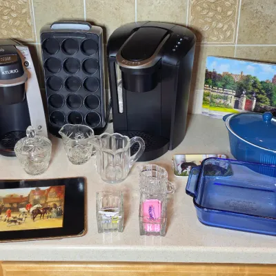 Assorted kitchenware including two Keurig coffee makers, a K-cup holder, blue glass baking dishes, and various glass serving pieces.