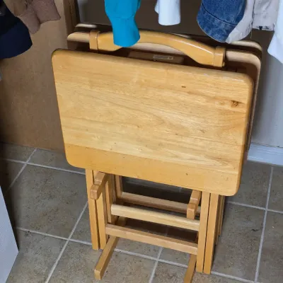 Set of four light oak folding TV tray tables stored on a matching wooden stand.